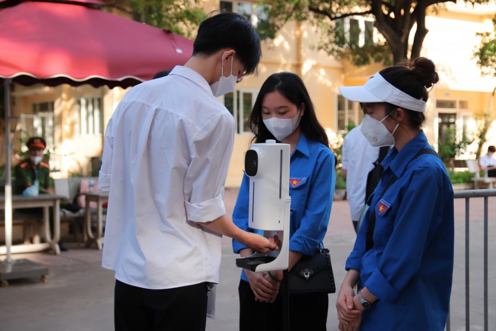 Tình nguyện viên nhắc nhở và hỗ trợ thí sinh rửa tay sát khuẩn trước khi vào điểm thi. (Ảnh: Trung Dũng)